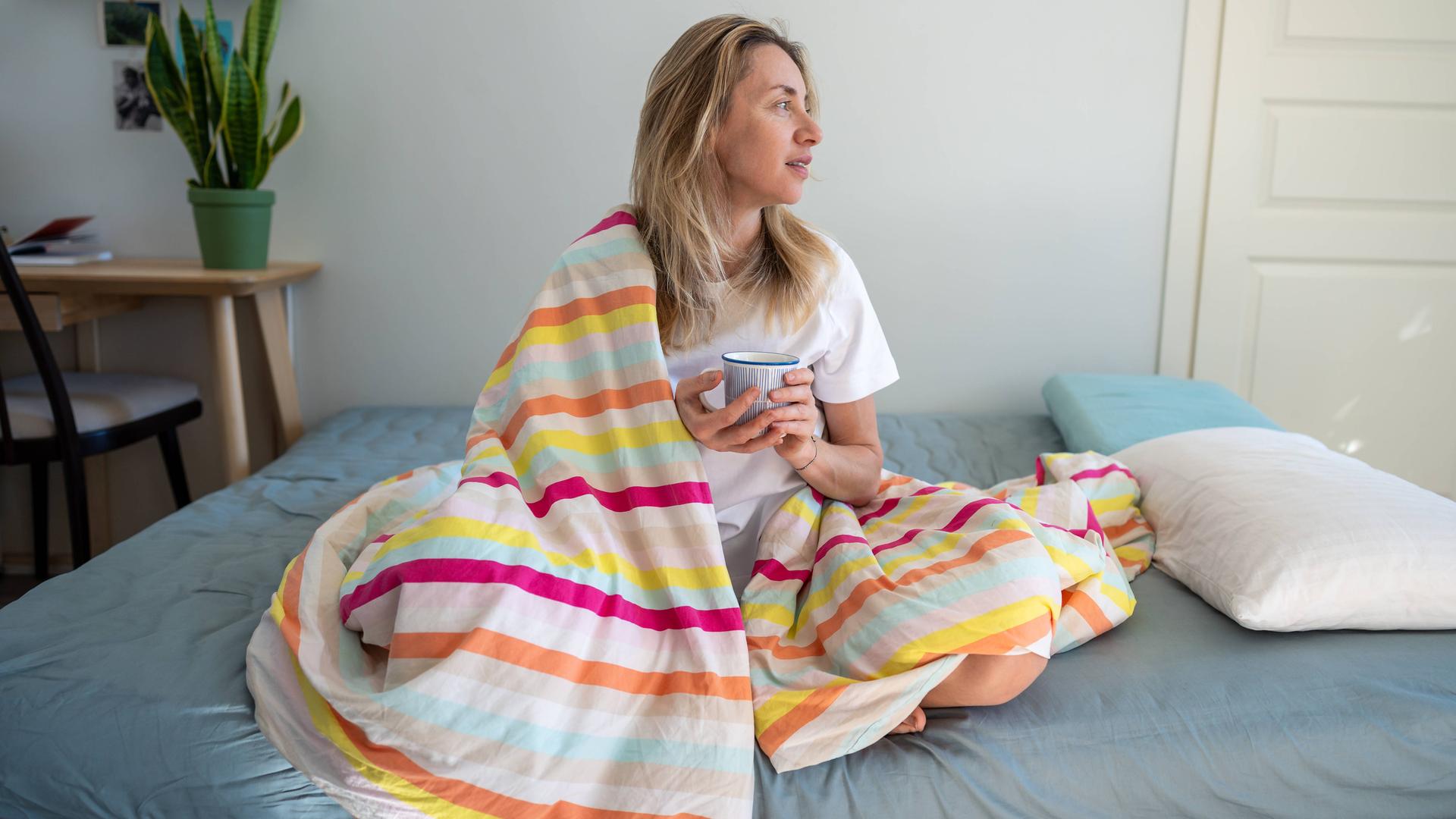 Entspannte Frau im Bett, die Kaffee genießt und sich an einem faulen Morgen ausruht.