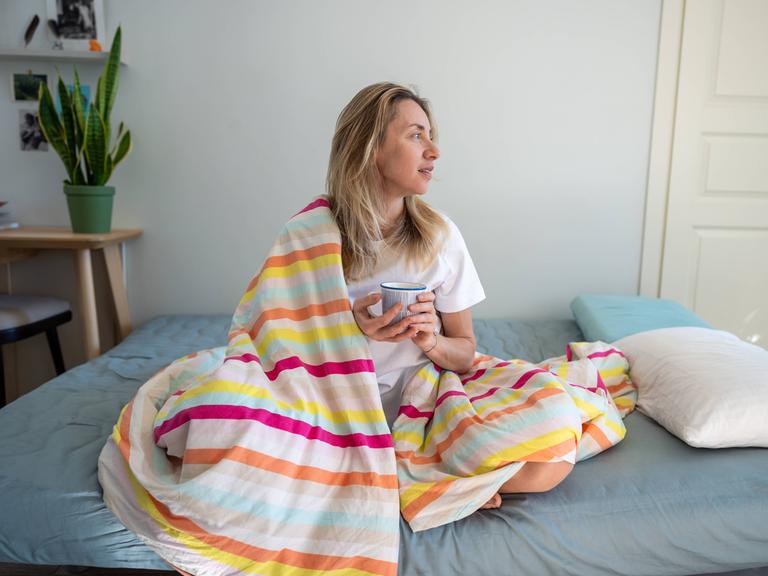 Entspannte Frau im Bett, die Kaffee genießt und sich an einem faulen Morgen ausruht.