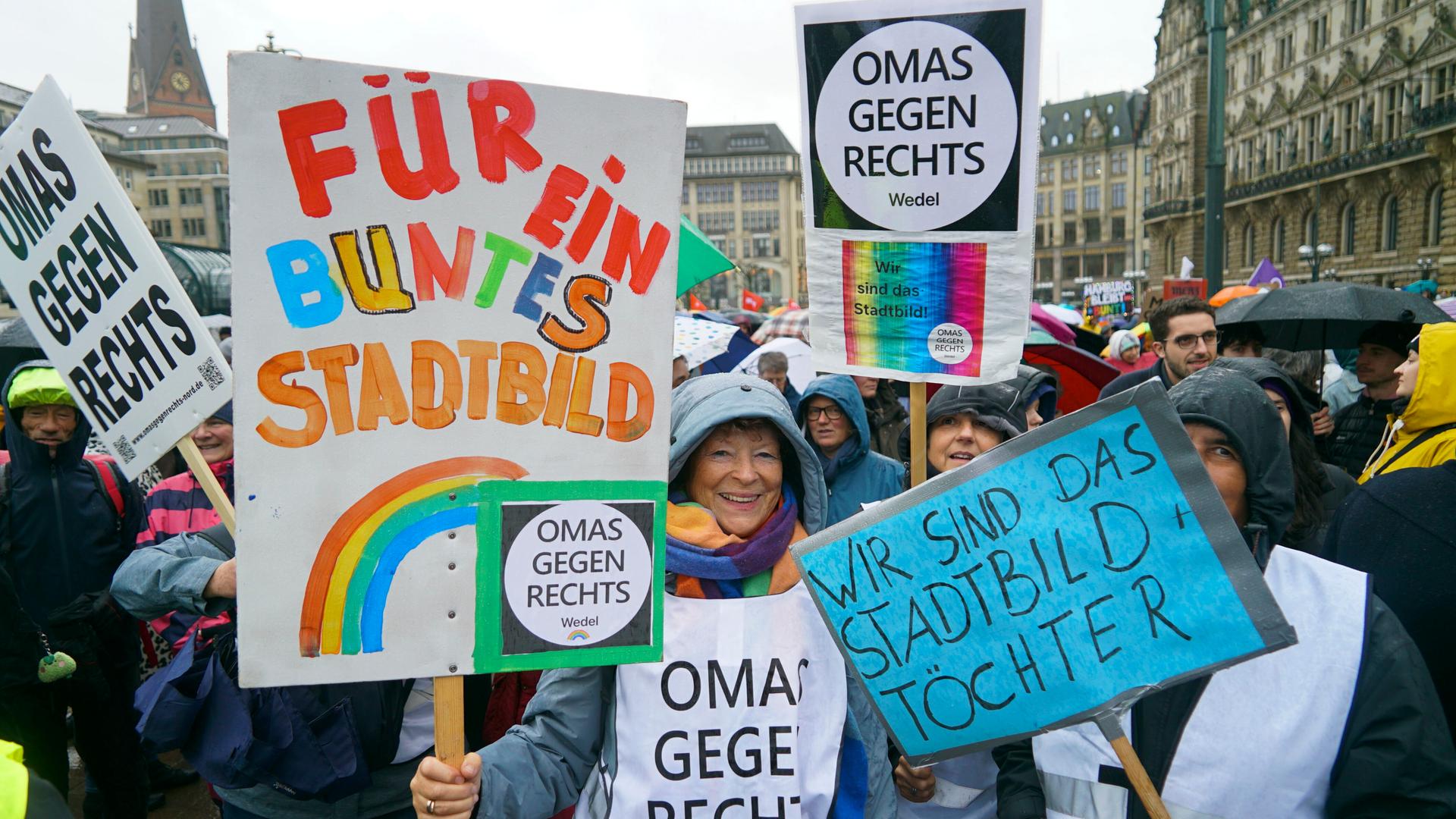 Mehrere Menschen stehen im Regen. Sie halten Plakate in die Höhe. Auf einem Plakat steht: "Für ein buntes Stadtbild" Mehrere Menschen stehen im Regen. Sie halten Plakate in die Höhe. Auf einem Plakat steht: "Für ein buntes Stadtbild"
