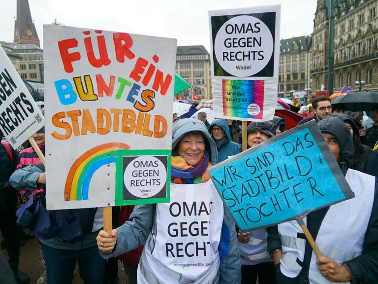 Mehrere Menschen stehen im Regen. Sie halten Plakate in die Höhe. Auf einem Plakat steht: "Für ein buntes Stadtbild" Mehrere Menschen stehen im Regen. Sie halten Plakate in die Höhe. Auf einem Plakat steht: "Für ein buntes Stadtbild"