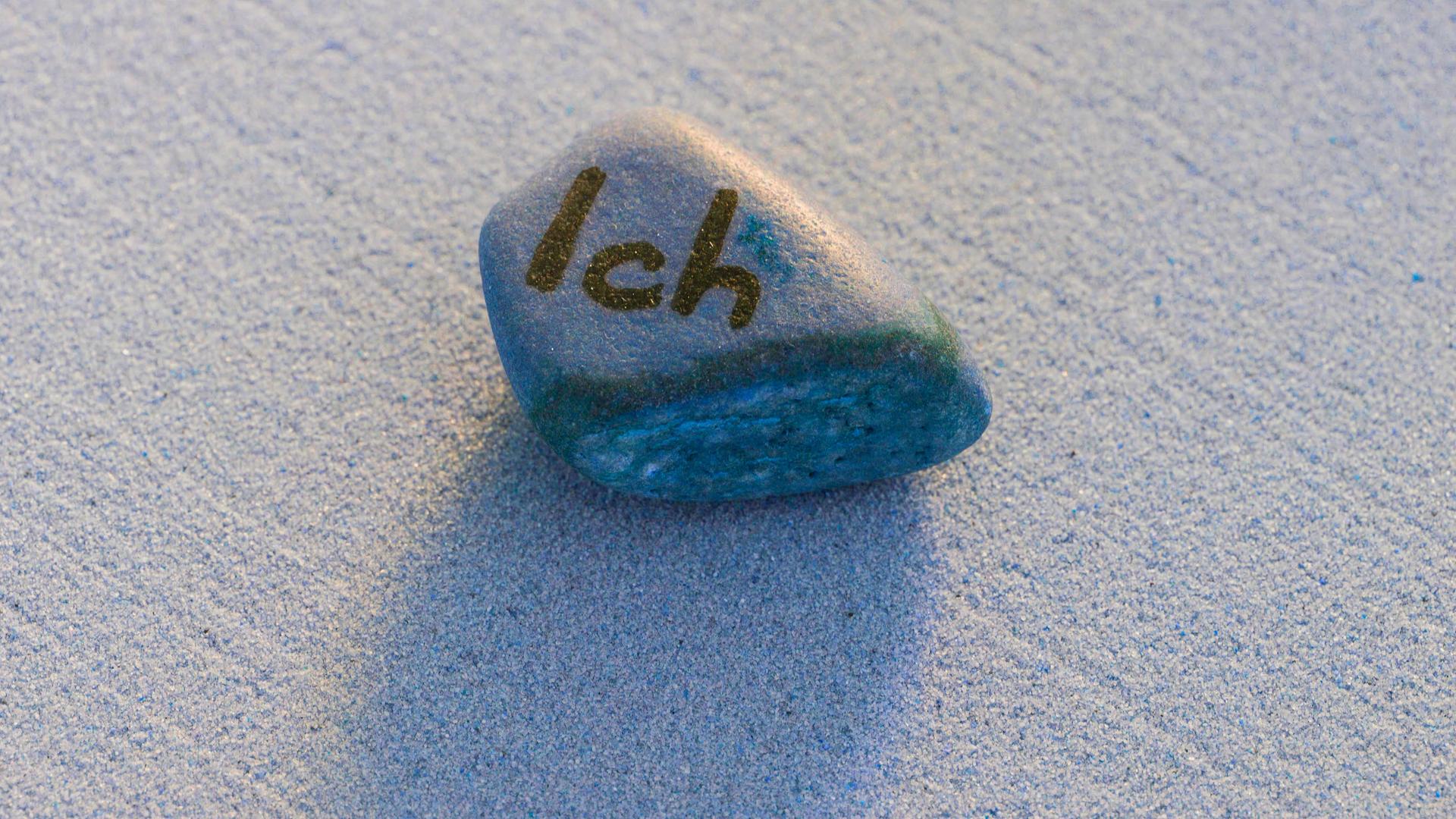 Ein grauer Stein mit der Aufschrift Ich auf Sand liegend.