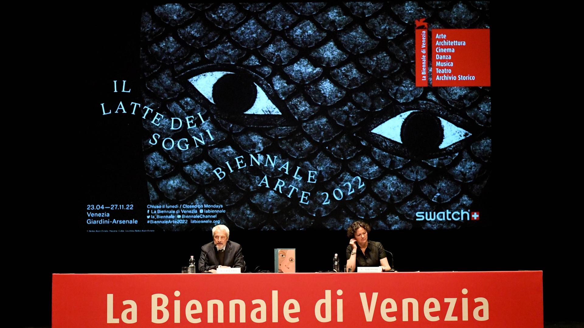 Auf dem Podium bei der Pressekonferenz der 59. Kunstbiennale Venedig sitzen Biennale-Präsident Roberto Cicutto und Kuratorin Cecilia Alemani vor einem großen Biennale-Plakat