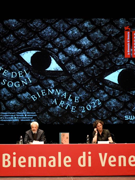 Auf dem Podium bei der Pressekonferenz der 59. Kunstbiennale Venedig sitzen Biennale-Präsident Roberto Cicutto und Kuratorin Cecilia Alemani vor einem großen Biennale-Plakat