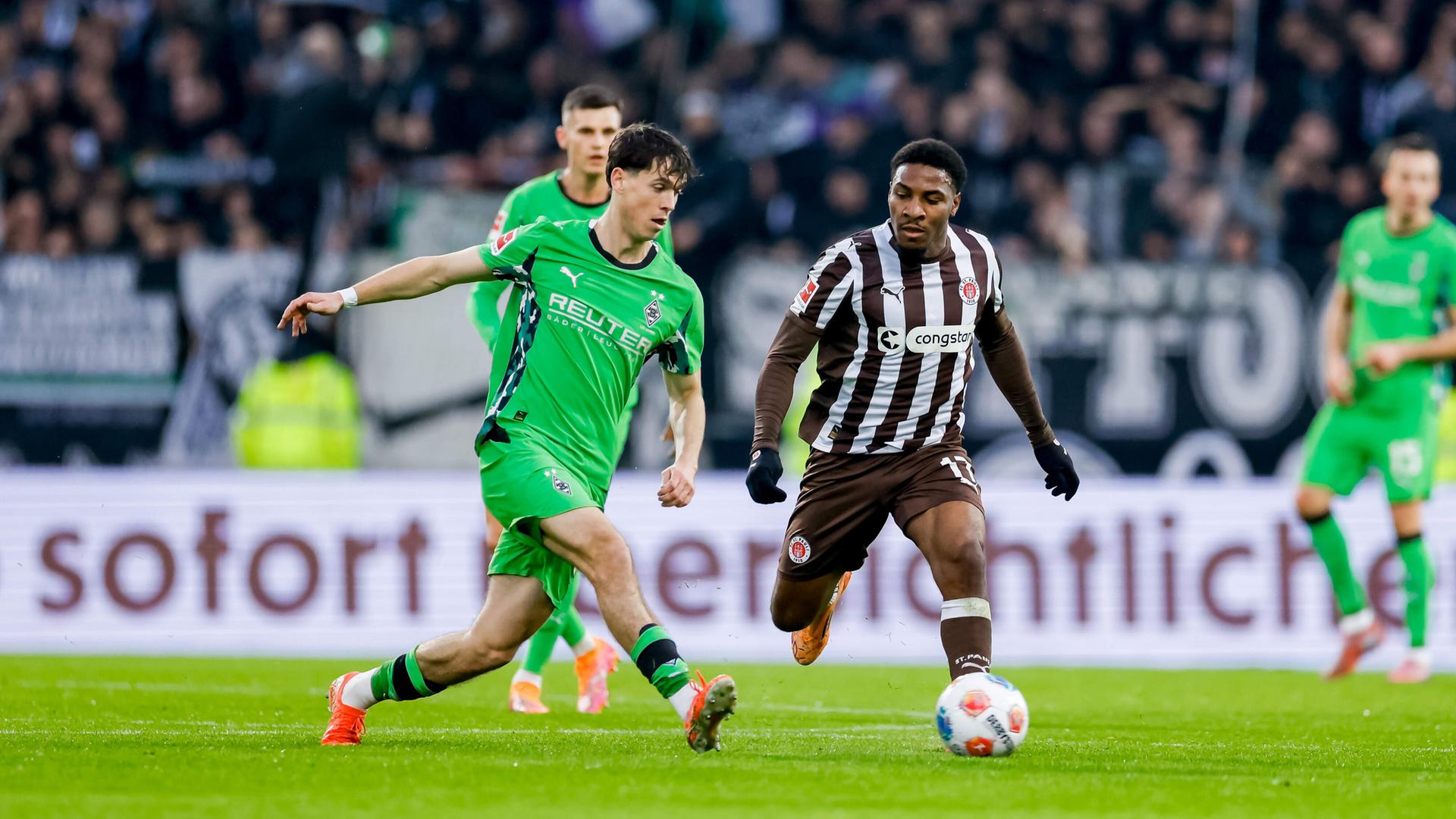 Philipp Sander im grünen Gladbach-Trikot kämpft mit Oladapo Afolayan im braun-weißen St.-Pauli-Trikot um den Ball. 
