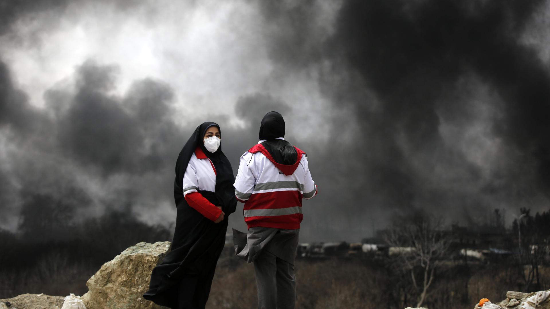 Zwei Personen stehen auf einer Annöhe und sehen schwarzer Rauch aufsteigen nach einem Angriff in Tehran.