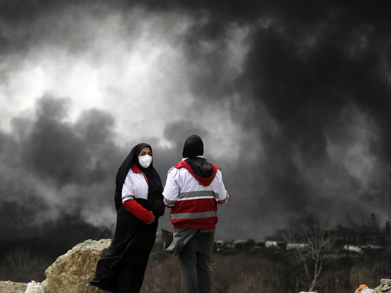Zwei Personen stehen auf einer Annöhe und sehen schwarzer Rauch aufsteigen nach einem Angriff in Tehran.