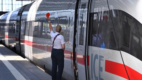 Eine Mitarbeiterin der Bahn gibt vor einem stehenden ICE das Zeichen zur Abfahrt