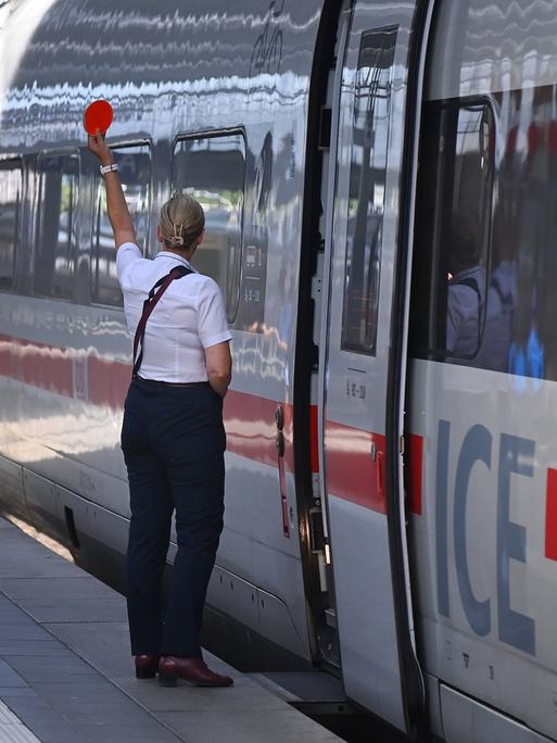 Eine Mitarbeiterin der Bahn gibt vor einem stehenden ICE das Zeichen zur Abfahrt Eine Mitarbeiterin der Bahn gibt vor einem stehenden ICE das Zeichen zur Abfahrt