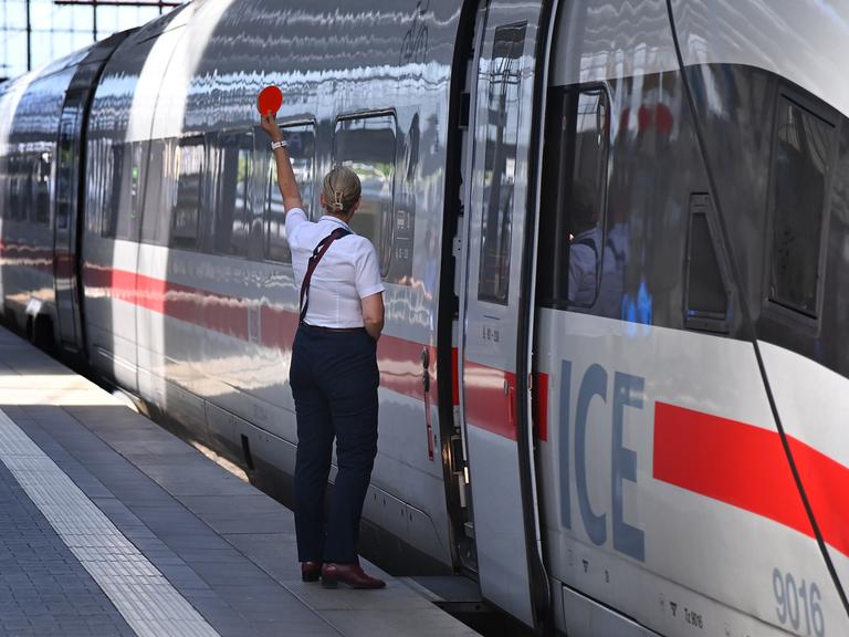Eine Mitarbeiterin der Bahn gibt vor einem stehenden ICE das Zeichen zur Abfahrt Eine Mitarbeiterin der Bahn gibt vor einem stehenden ICE das Zeichen zur Abfahrt