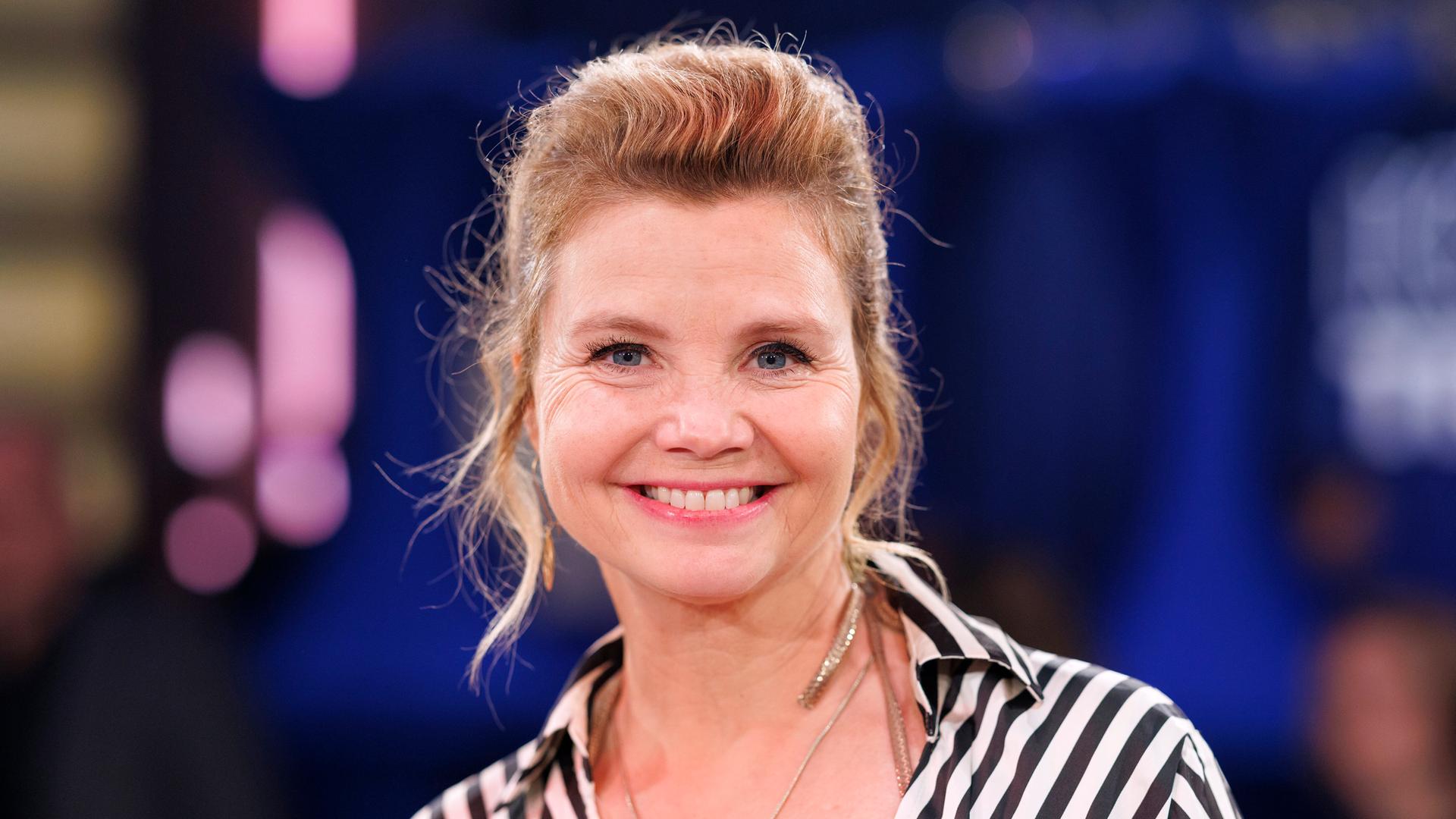 Schauspielerin Annette Frier trägt eine schwarzweiss gestreifte Bluse und lacht in die Kamera.