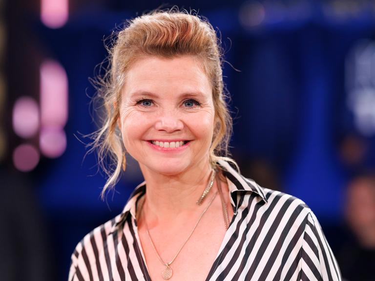 Schauspielerin Annette Frier trägt eine schwarzweiss gestreifte Bluse und lacht in die Kamera.