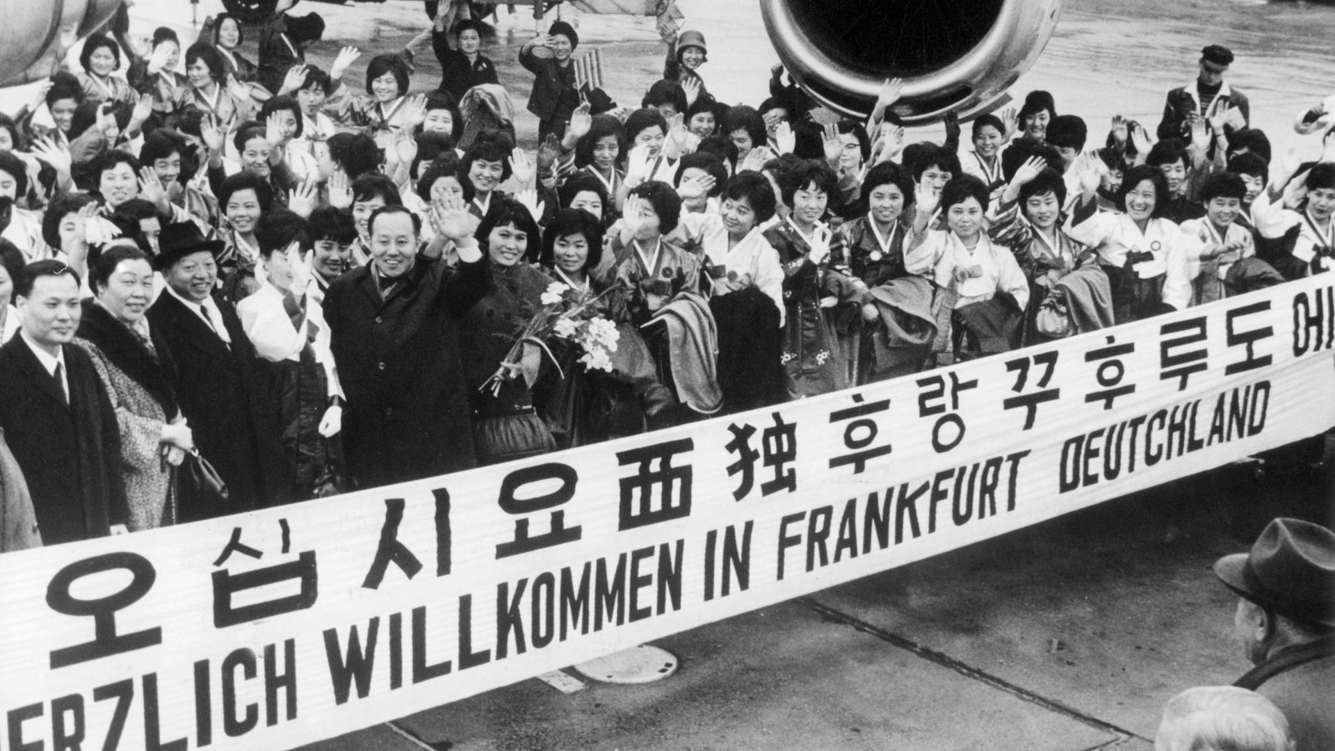 "Herzlich Willkommen in Frankfurt Deutschland" steht auf einem Spruchband, mit dem eine Gruppe Krankenschwestern aus Südkorea im Jahr 1966 auf dem Rhein-Main-Flughafen begrüsst wird. In Deutschland herrscht ein mangel an Pflegepersonal und Krankenschwestern.