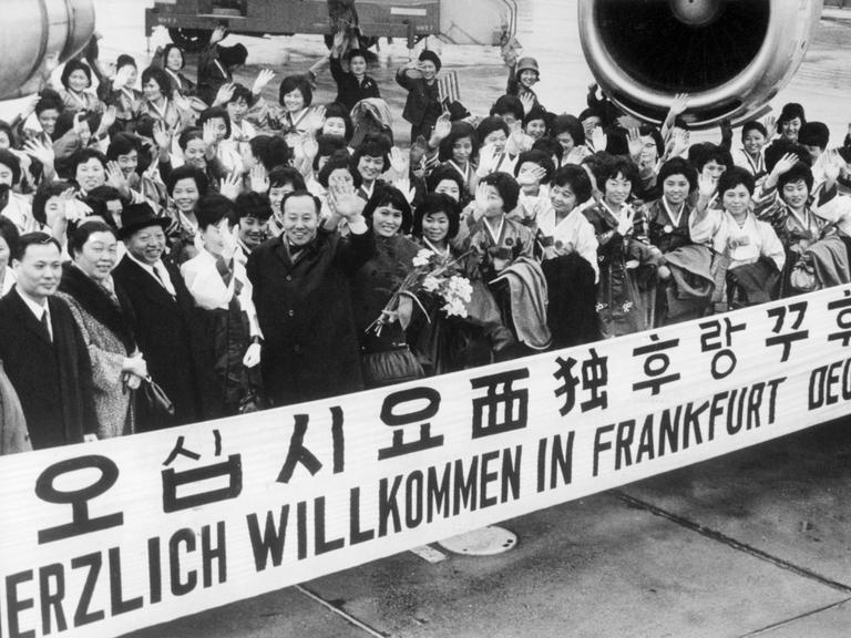 "Herzlich Willkommen in Frankfurt Deutschland" steht auf einem Spruchband, mit dem eine Gruppe Krankenschwestern aus Südkorea im Jahr 1966 auf dem Rhein-Main-Flughafen begrüsst wird. In Deutschland herrscht ein mangel an Pflegepersonal und Krankenschwestern.