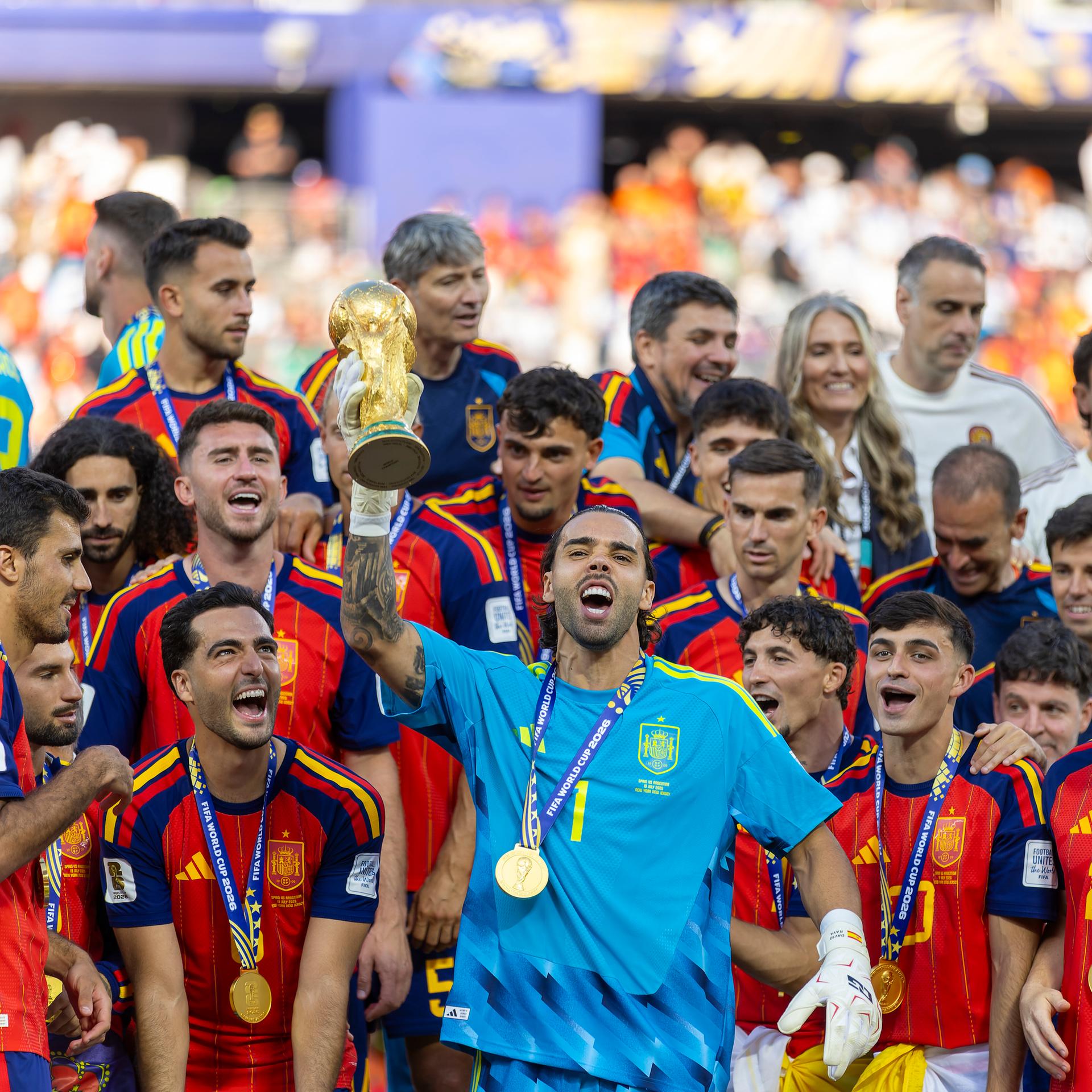 Der spanische National-Torhüter David Raya reckt nach dem Sieg über Argentinien im Endspiel der Fußball-Weltmeisterschaft den Pokal in die Höhe. Er ist umringt von seinen Team-Kollegen.