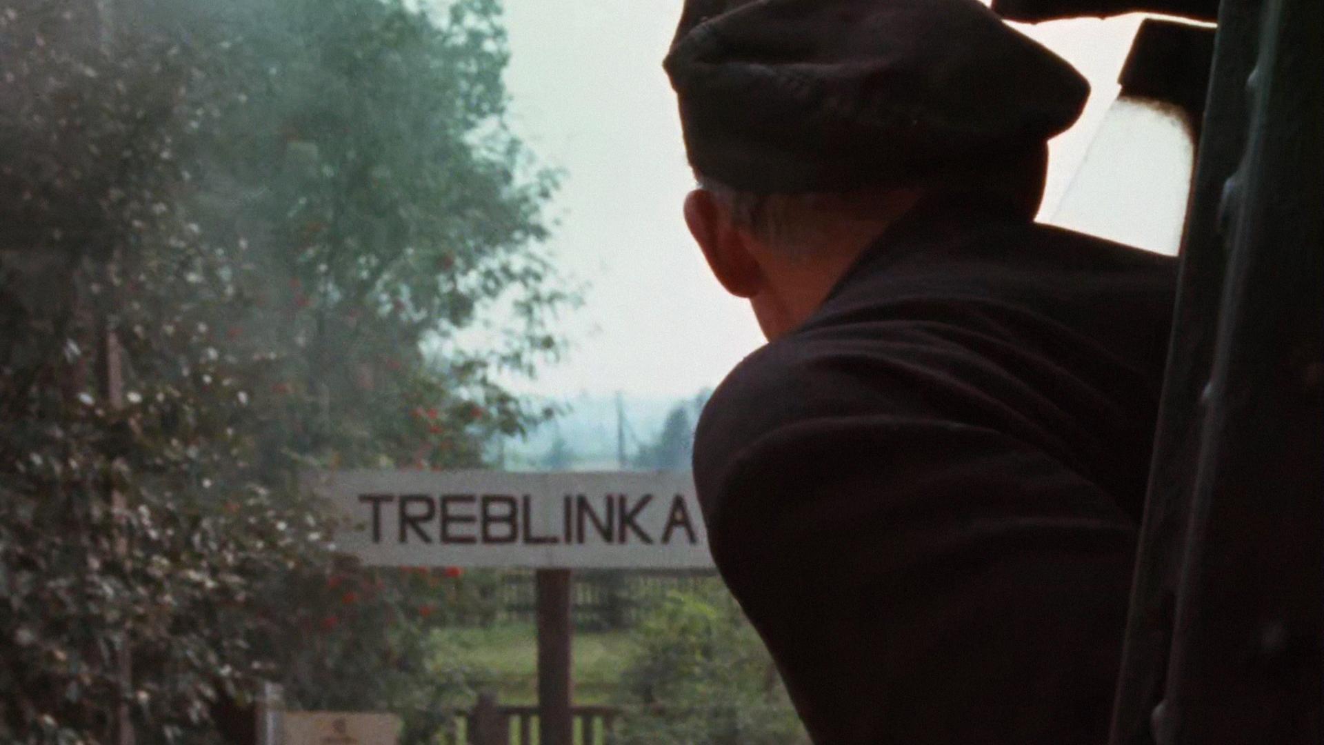 Szene aus Claude Lanzmanns Shoa. Eine Person guckt aus einem Zug, während dieser ein Schild mit der Aufschrift "Treblinka" passiert. Szene aus Claude Lanzmanns Shoa. Eine Person guckt aus einem Zug, während dieser ein Schild mit der Aufschrift "Treblinka" passiert.