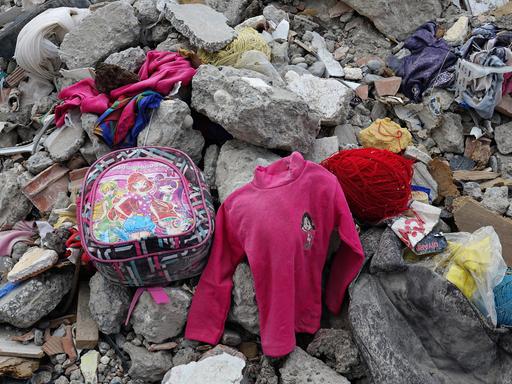 Zwischen den Trümmern eines zerstörten Hauses liegen nach dem Erdbeben in der Türkei Kinderkleidung und ein Rucksack herum. 