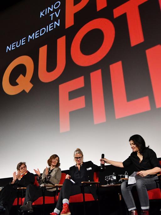 Mehrere Frauen sitzen nebeneinander vor einer Leinwand in einem Kinosaal. Auf der Leinwand steht "Quote Film".