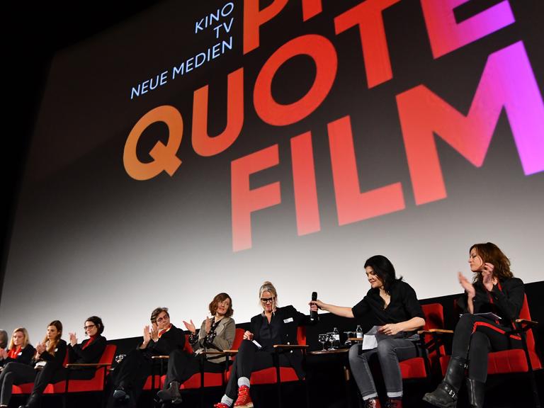 Mehrere Frauen sitzen nebeneinander vor einer Leinwand in einem Kinosaal. Auf der Leinwand steht "Quote Film".