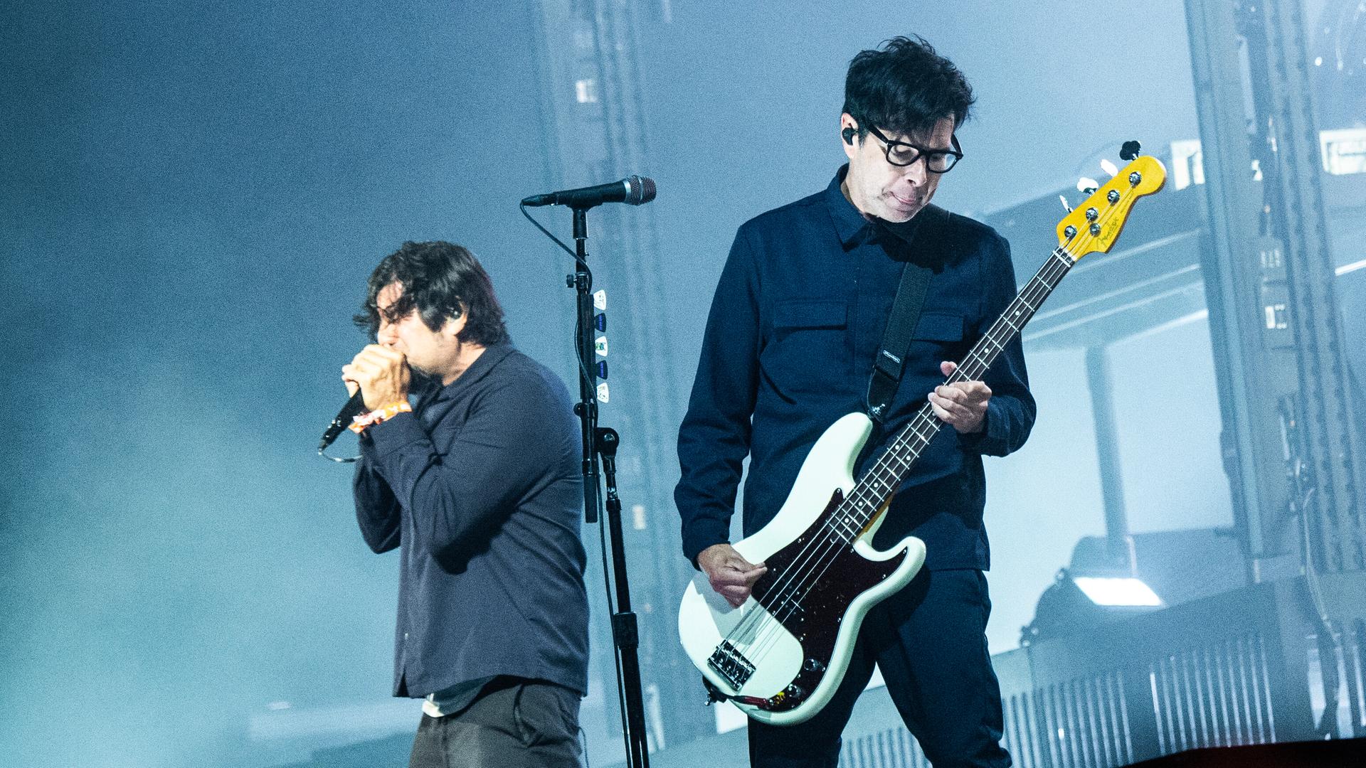 Sänger und Gitarrist der Band Deftones performen auf eine blau ausgeleuchteten Bühne. 