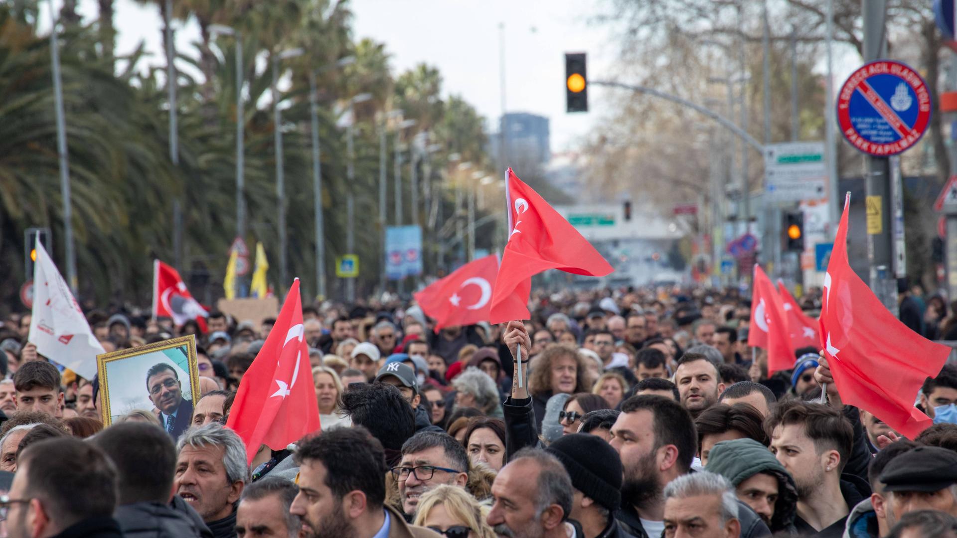 Menschen auf der Straße in Istanbul. Sie haben Türkei-Fahnen und ein Bild von Imamoglu dabei.