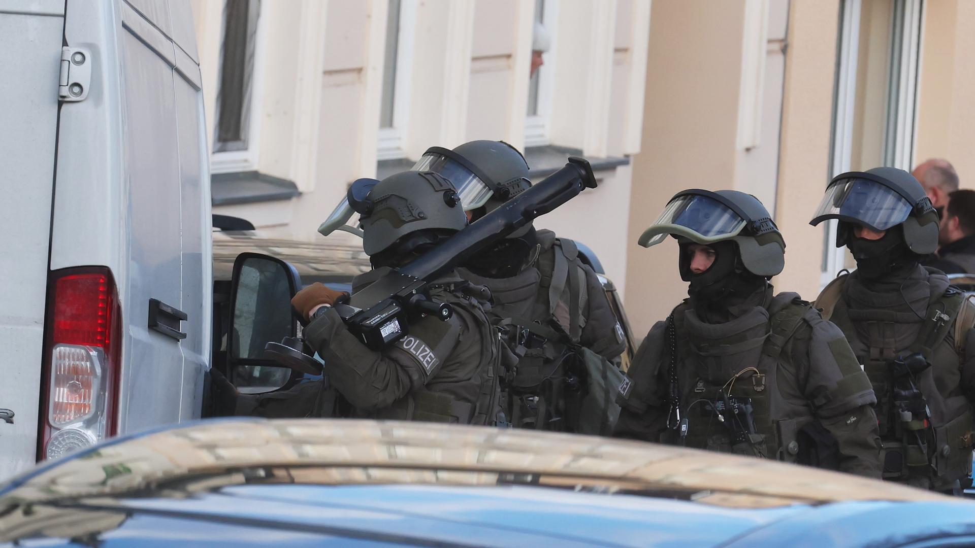 Polizisten mit Helmen und einer Ramme. Man sieht sie hinter zwei Fahrzeugen. 