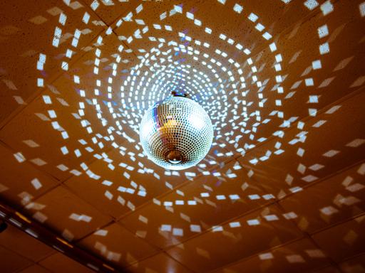 Eine Discokugel wirft zahlreiche Lichtreflexionen an eine Saaldecke.