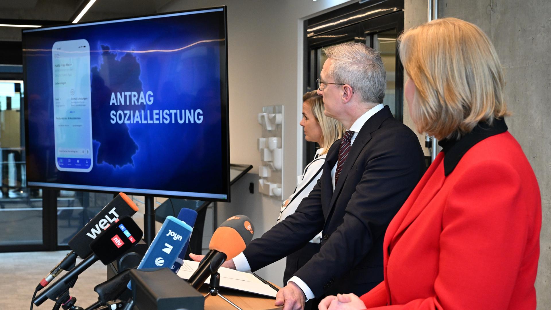 Bärbel Bas (r, SPD), Bundesministerin für Arbeit und Soziales, und Karsten Wildberger (CDU), Bundesminister für Digitalisierung und Staatsmodernisierung (BMDS), verfolgen gemeinsam mit BMDS-Sprecherin Betty Kieß (l) eine Videopräsentation.