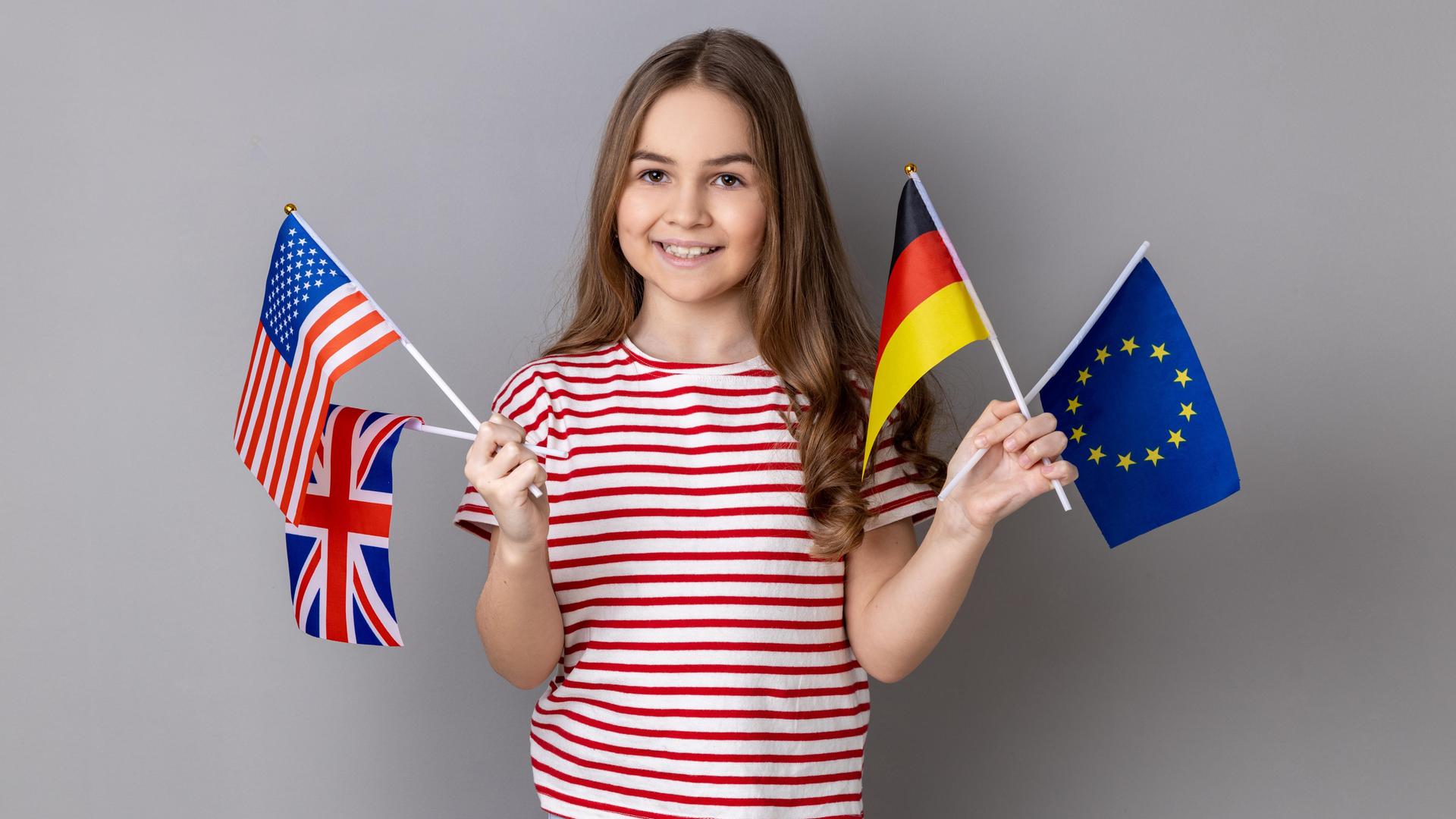 Ein lächelndes Mädchen hält die Fahnen Deutschlands, Großbritanniens, der USA und der Europäischen Union.