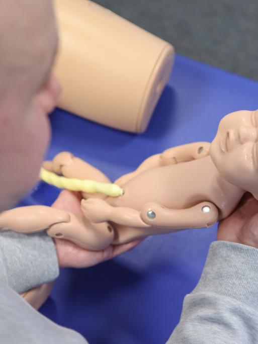 Eine männliche Hebamme, hält in einer gestellten Situation eine Neugeborenen-Übungspuppe mit Nabelschnur. Eine männliche Hebamme, hält in einer gestellten Situation eine Neugeborenen-Übungspuppe mit Nabelschnur.