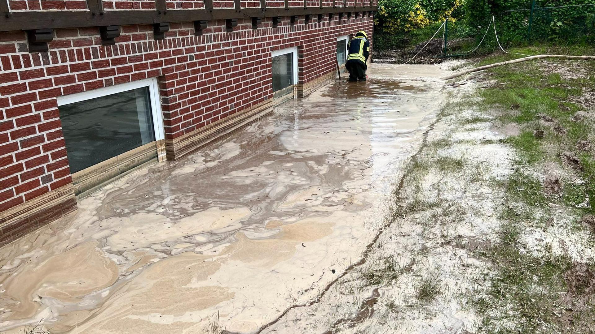 Niedersachsen, Georgsmarienhütte: Ein Feuerwehrmann pumpt Regenwasser aus der Grube vor einem Wohnhaus.