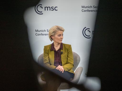 Ursula von der Leyen, Präsidentin der Europäischen Kommission, während der Münchner Sicherheitskonferenz. Sie schaut nachdenklich zur Seite, ihr Konterfei ist eingerahmt von dunklen Rändern. Der Fotograf hat offenbar zwischen anderen Menschen hindurch fotografiert. 