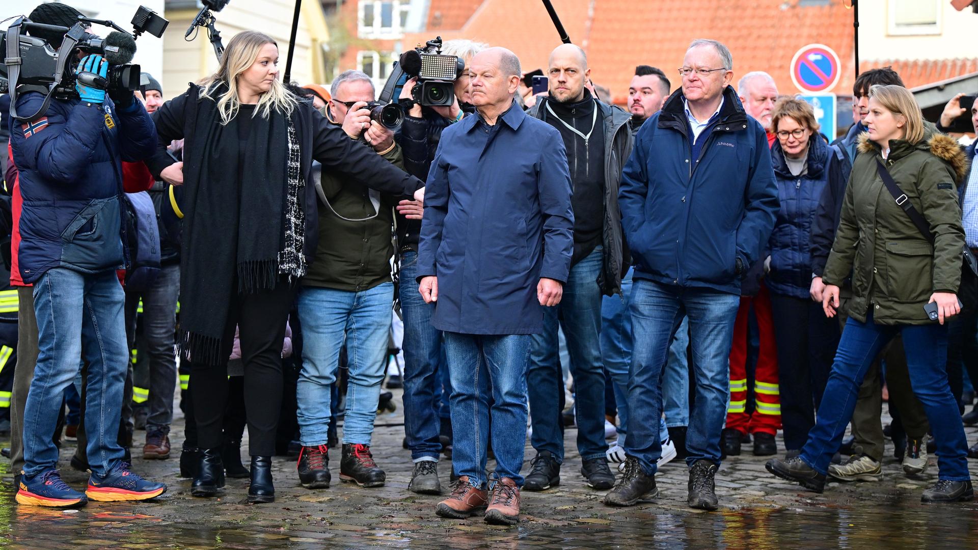Bundeskanzler Olaf Scholz (SPD, M) und Stephan Weil (SPD, Mitte r), Ministerpräsident von Niedersachsen, stehen bei ihrem Besuch im Hochwassergebiet am Zusammenfluss von Weser und Aller an einer überfluteten Straße