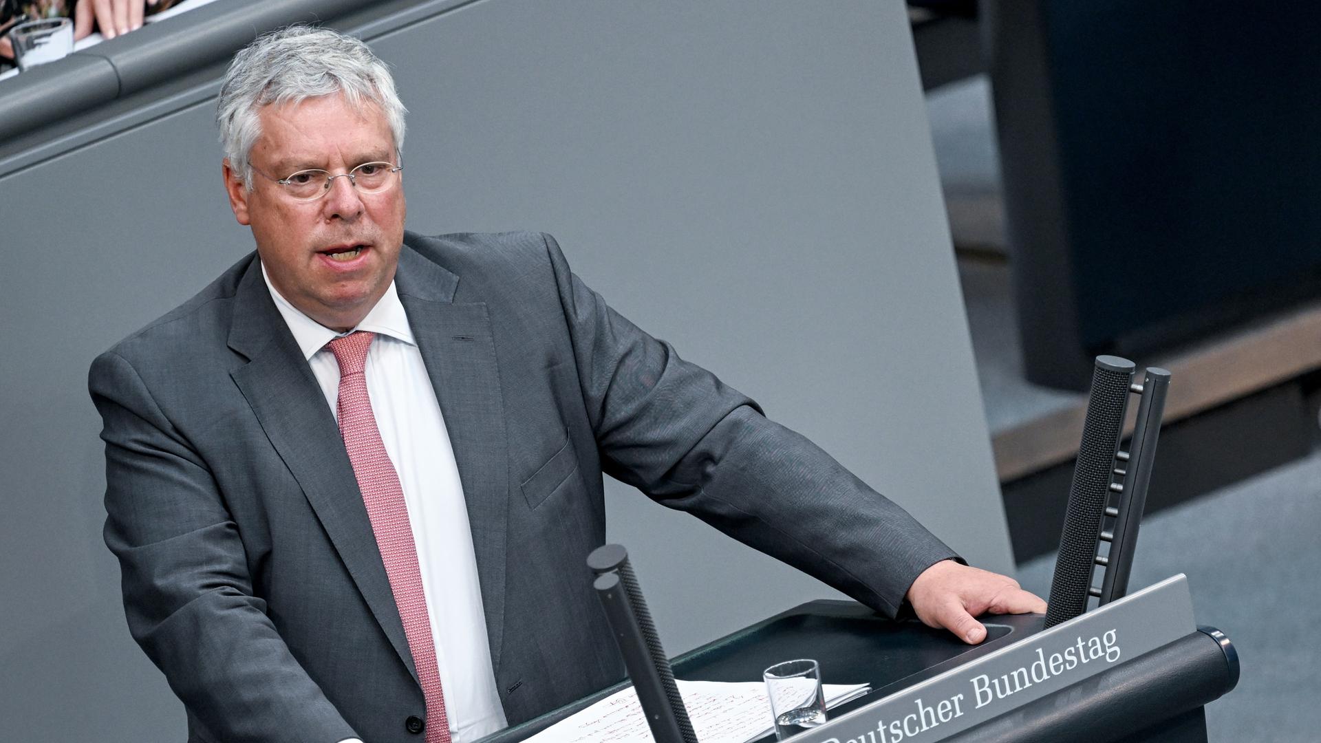 Hardt im grauen Jackett mit roter Krawatte und weißem Hemd am Rednerpult des Bundestags.