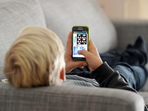 Ein Jugendlicher schaut auf sein Smartphone. Er liegt dabei auf dem Sofa und ist nur von hinten zu sehen. Ein Jugendlicher schaut auf sein Smartphone. Er liegt dabei auf dem Sofa und ist nur von hinten zu sehen.
