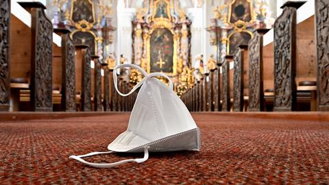 Symbolbild zum Kirchenbesuch während der Coronapandemie, auf dem Kirchenboden liegt eine FFP2-Maske
