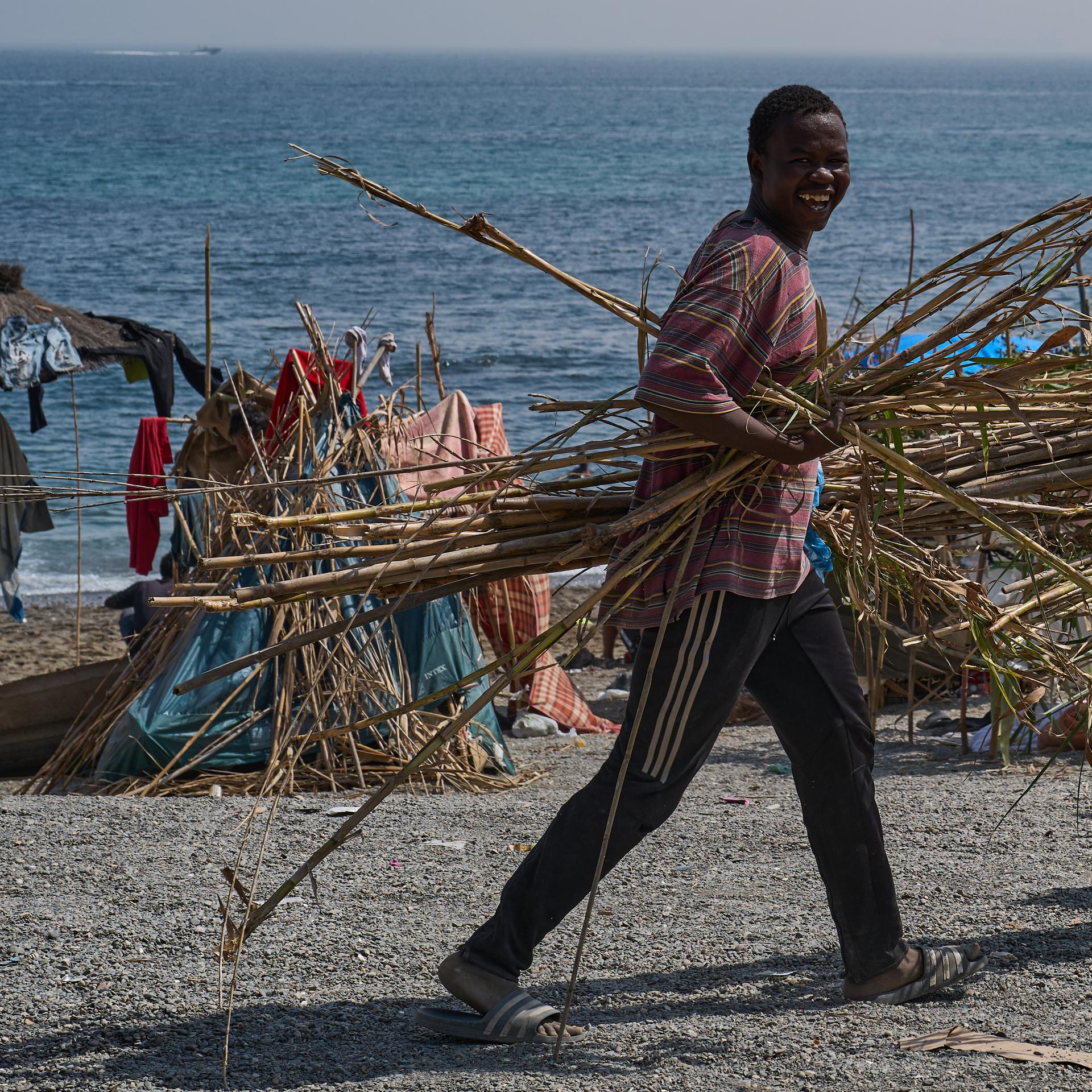 Ein fröhlich lachender Mann trägt Holz an einem Strand