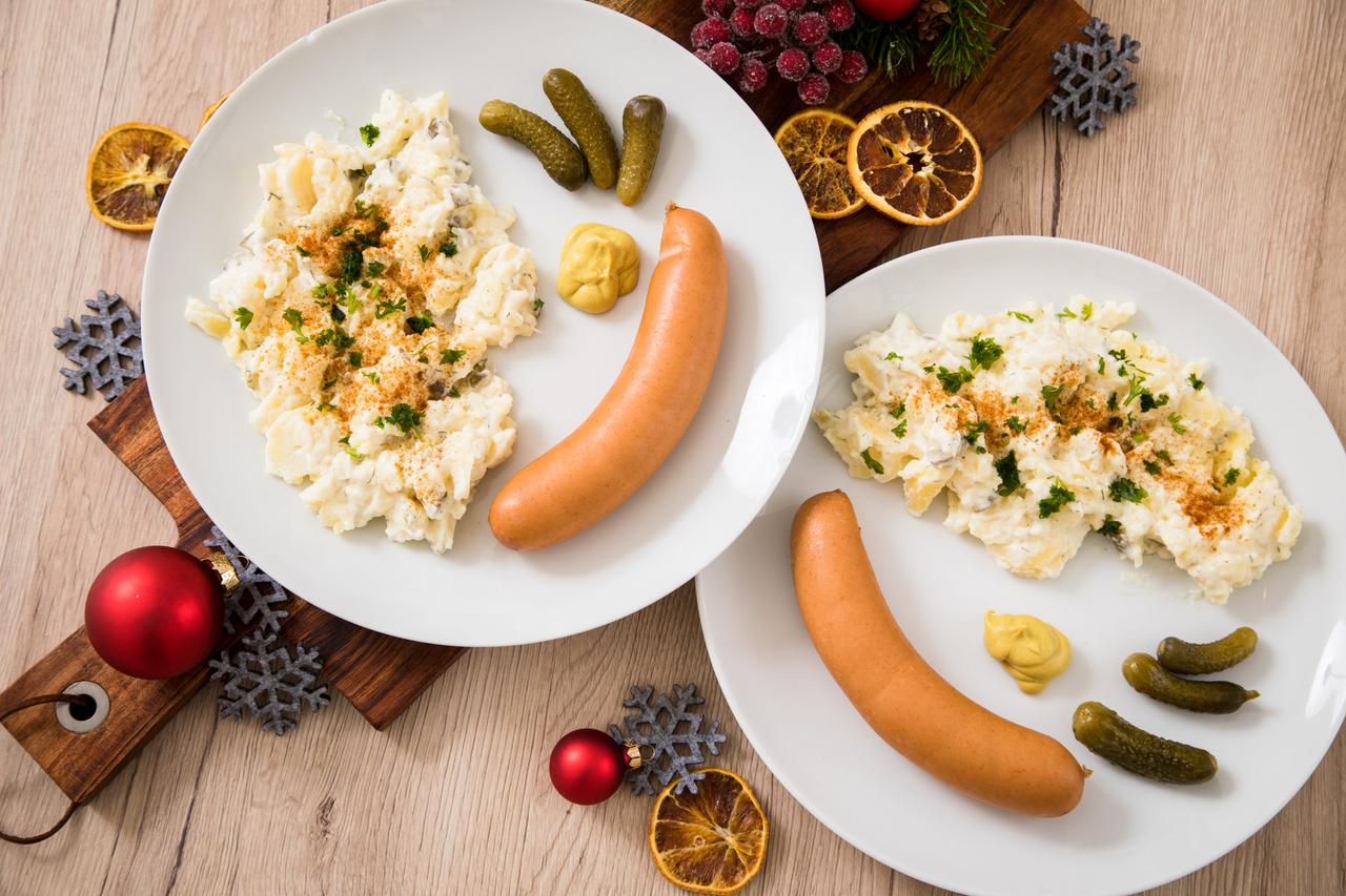 Kartoffelsalat mit Würstchen sind auf Tellern angerichtet (gestellte Szene)