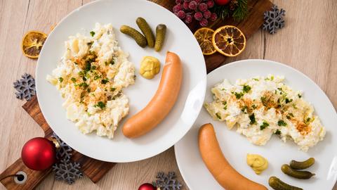 Kartoffelsalat mit Würstchen sind auf Tellern angerichtet (gestellte Szene)