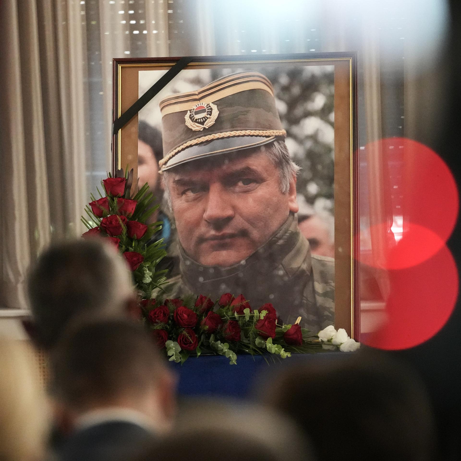 Ein Porträt des bosnisch-serbischen Kriegsverbrechers Ratko Mladić in Uniform ist in einem Rahmen aufgestellt. Vor dem Rahmen ist ein Bouquet roter Rosen angebracht. 
