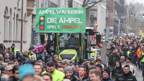 Teilnehmer einer Protestaktion gehen neben einem Traktor, an dem ein Schild mit der Aufschrift "Ampel-Wahnsinn - die Ampel spielt verrückt!" angebracht ist.