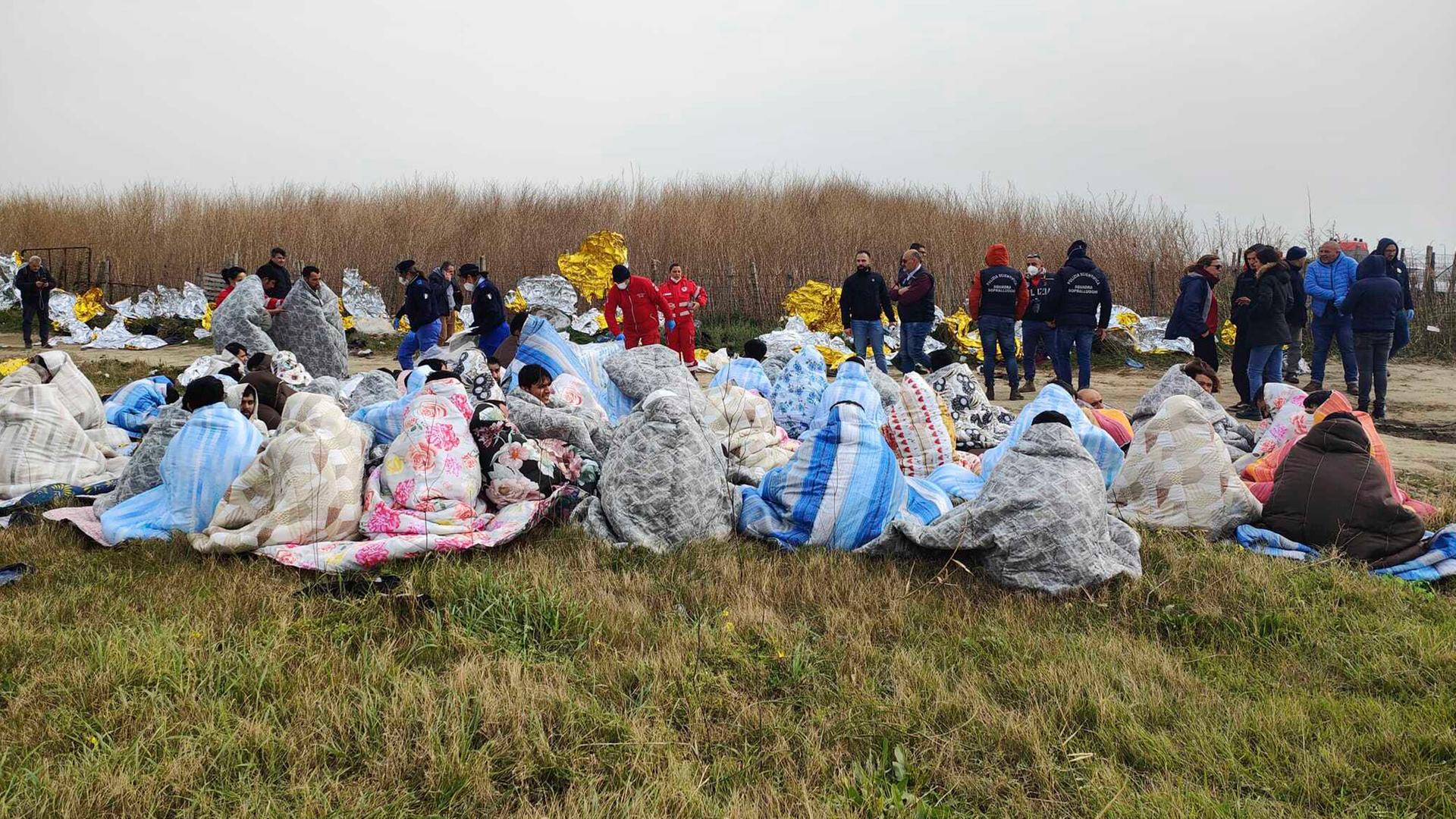 Gerettete Flüchtlinge sitzen in Decken gehüllt an einem Strand in der Nähe von Cutro in Süditalien.