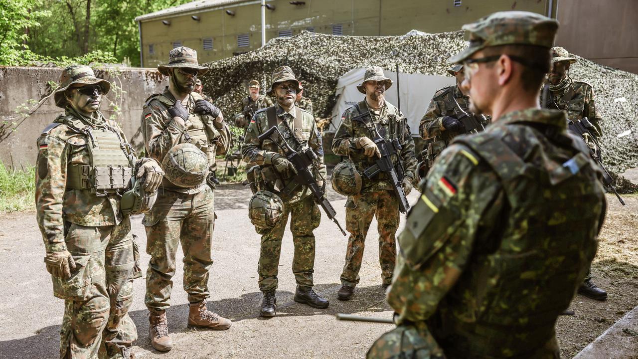 Ein Spähtrupp bestehend aus sechs Mann in Tarnuniform nimmt einen Befehl entgegen.