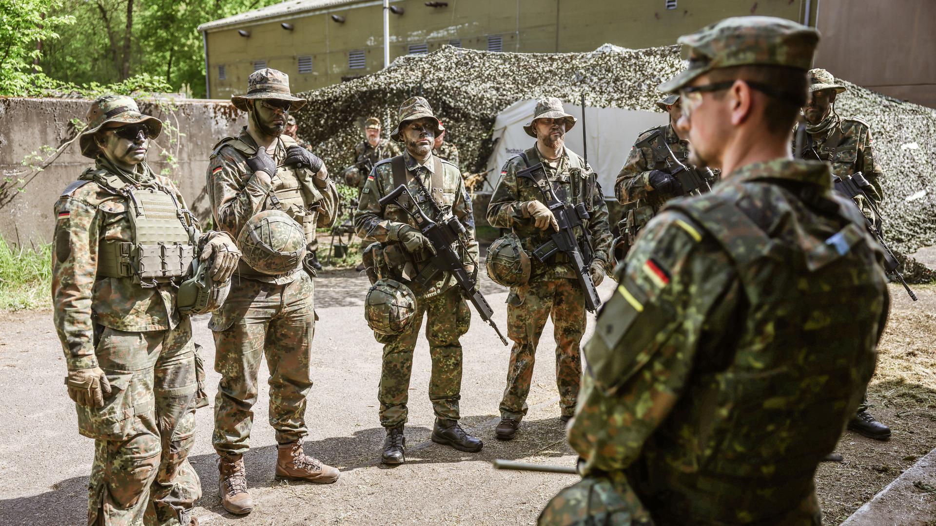 Ein Spähtrupp bestehend aus sechs Mann in Tarnuniform nimmt einen Befehl entgegen.