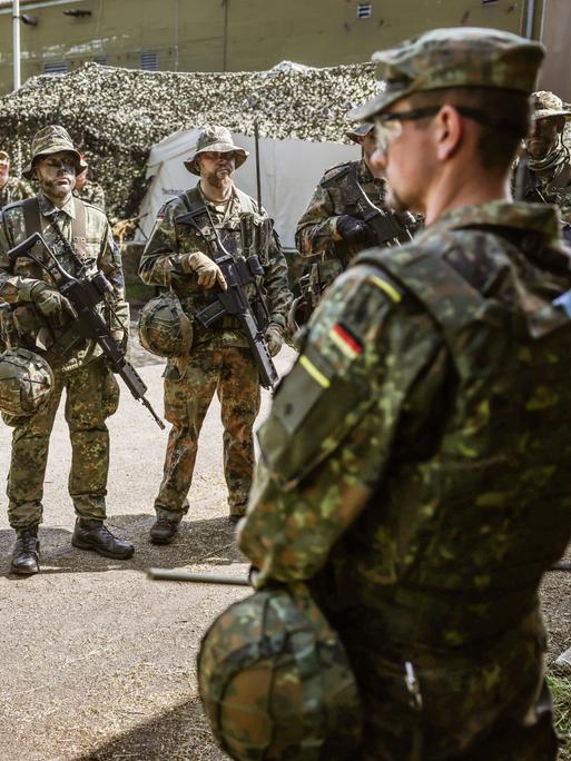 Ein Spähtrupp bestehend aus sechs Mann in Tarnuniform nimmt einen Befehl entgegen.