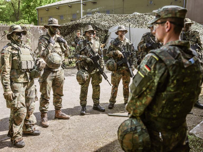 Ein Spähtrupp bestehend aus sechs Mann in Tarnuniform nimmt einen Befehl entgegen.