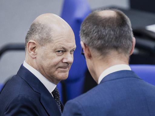 Bundeskanzler Olaf Scholz (SPD) und Friedrich Merz (CDU) begegnen sich im Bundestag und schauen sich an. 