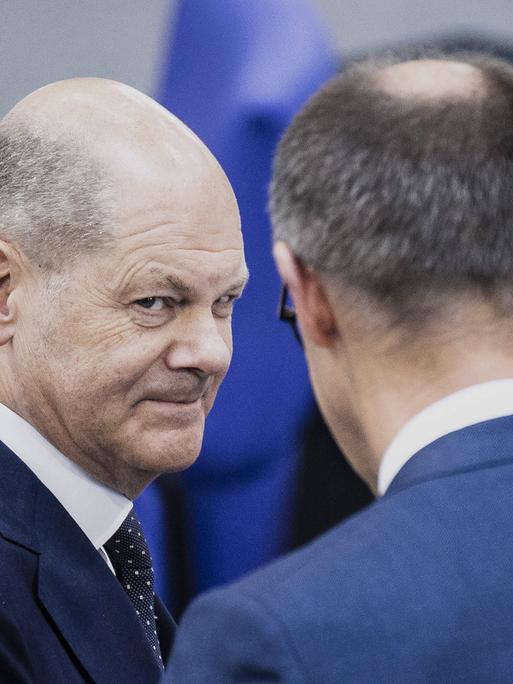 Bundeskanzler Olaf Scholz (SPD) und Friedrich Merz (CDU) begegnen sich im Bundestag und schauen sich an. 