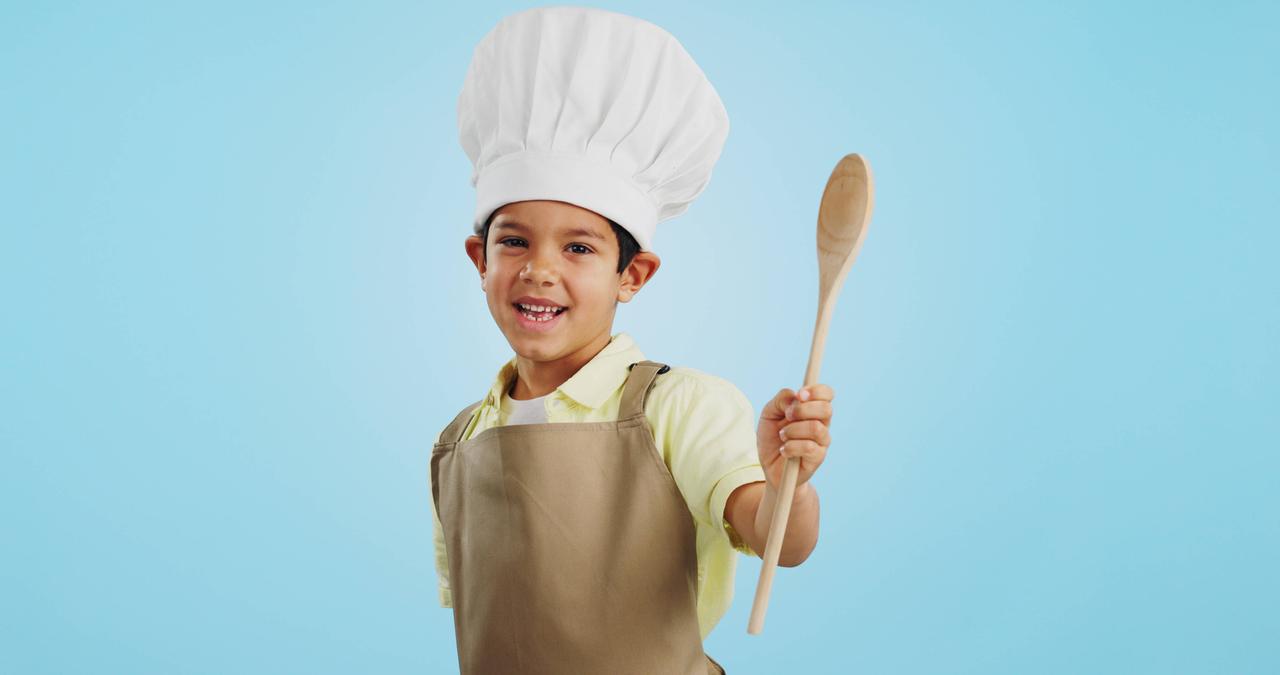 Junge mit einer weißen Kochmütze und einem Holzkochlöffel in der Hand. 