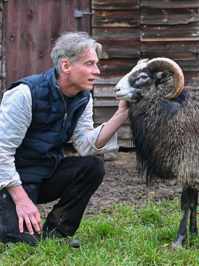 Holger Siemann, Bauer, Schriftsteller und Hörspielautor, hockt in seinem Garten in der Uckermark vor einem Gotlandschaf. 