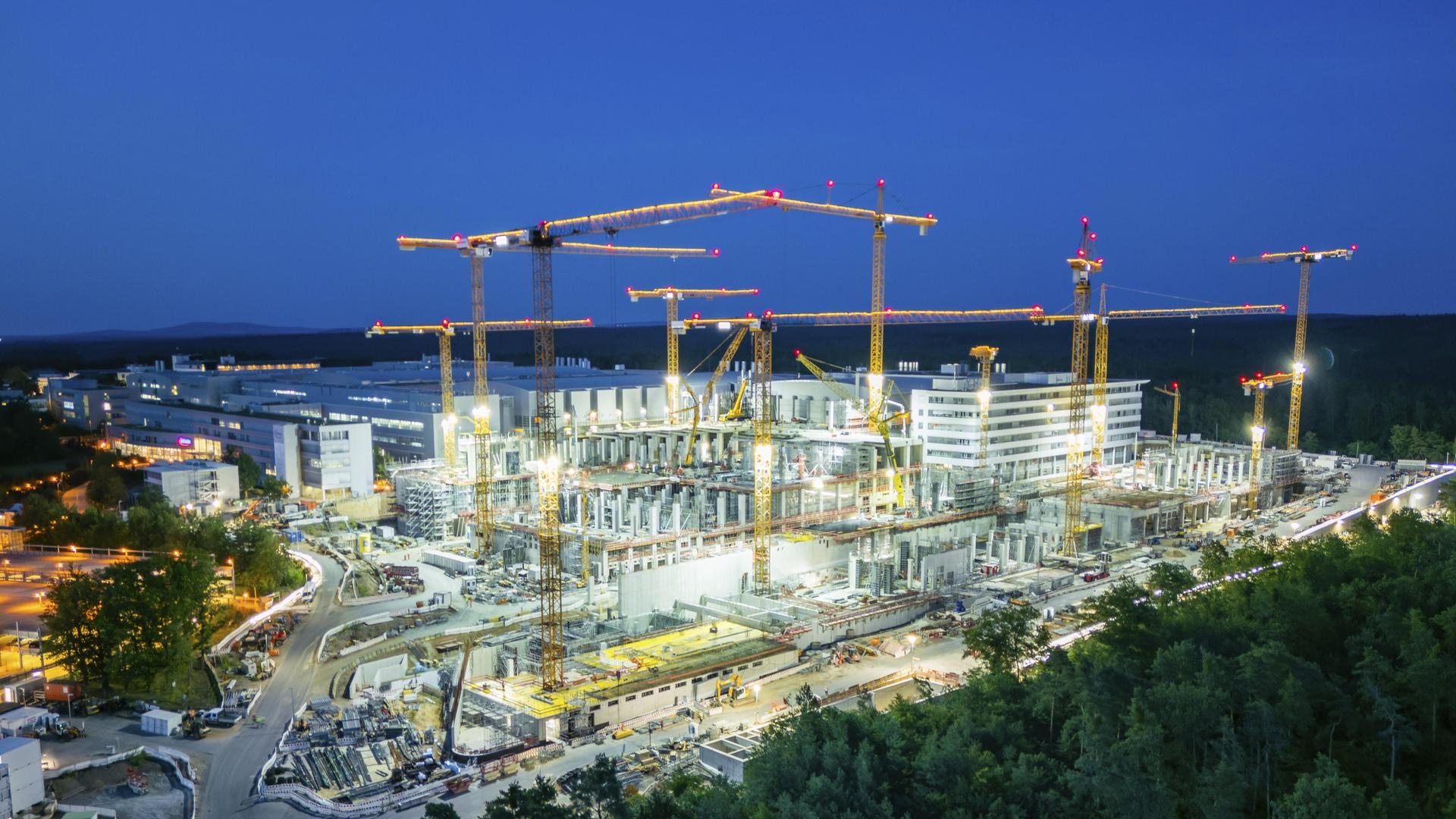 Beleuchtete Baustelle einer Fabrik umgeben von Wald. Nachtaufnahme. Luftaufnahme.